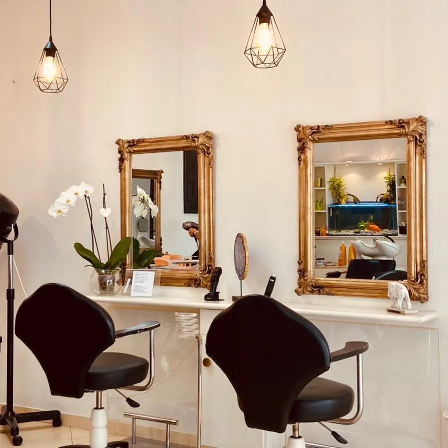 Interior do salão, com espelhos dourados e cadeiras de cabeleireiro